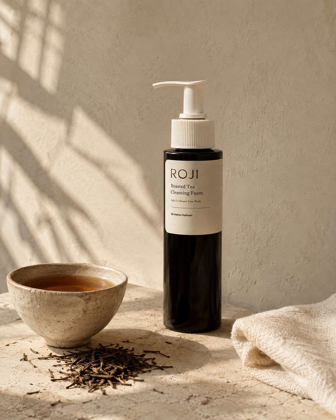 ROJI bottle concept with roasted tea, a ceramic cup, and an ivory washcloth in warm light