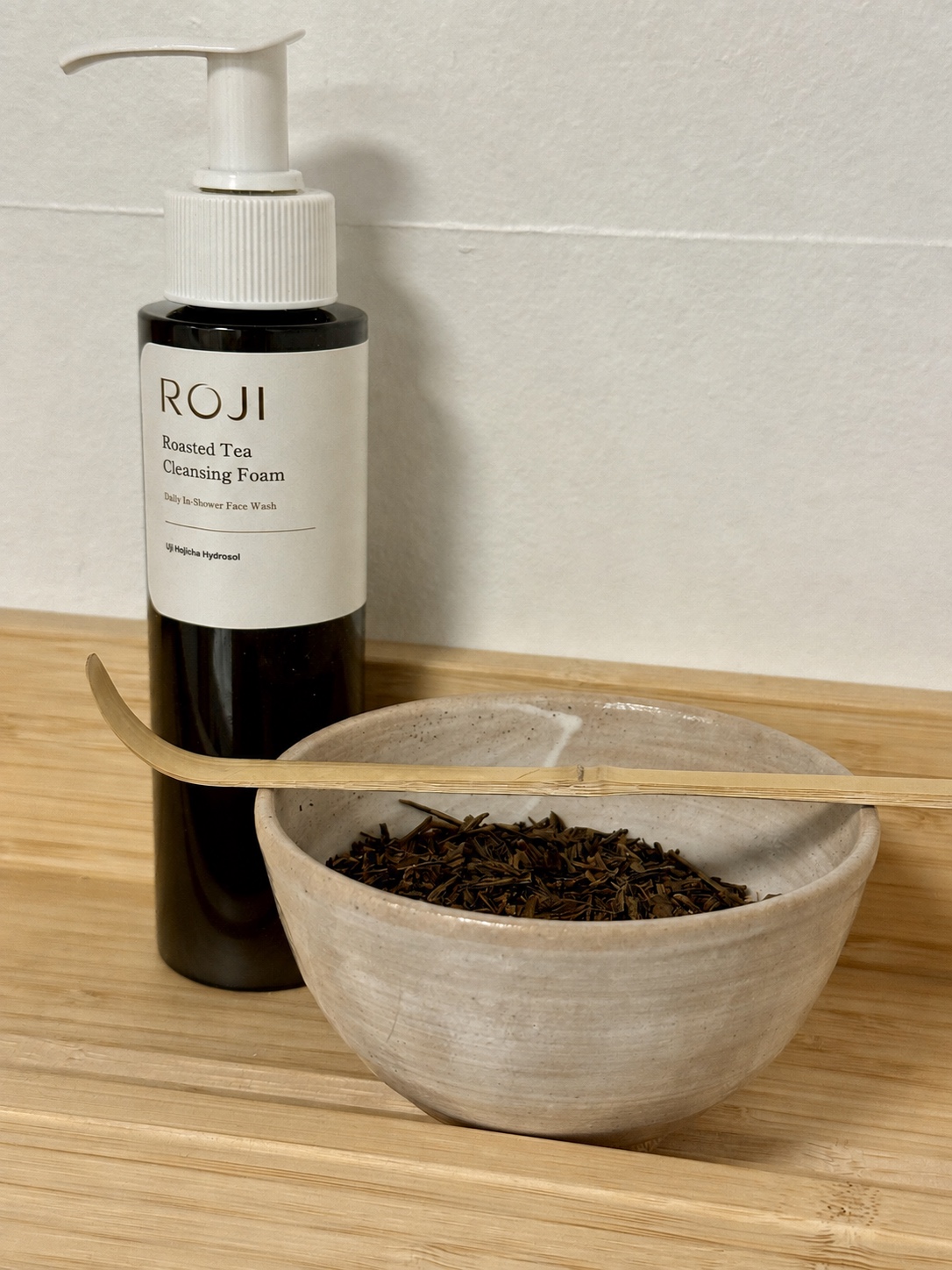 ROJI cleanser packaging concept beside a ceramic bowl of hojicha leaves and a bamboo scoop